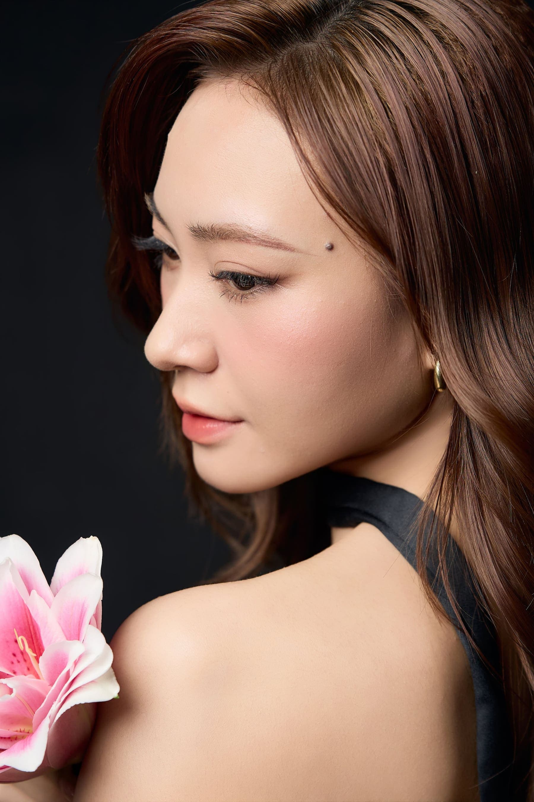 Người phụ nữ ôm bó hoa ly hồng, mắt khép nhẹ, gương mặt nghiêng vào hoa — một khoảnh khắc rất riêng giữa nhiều câu hỏi trong lòng