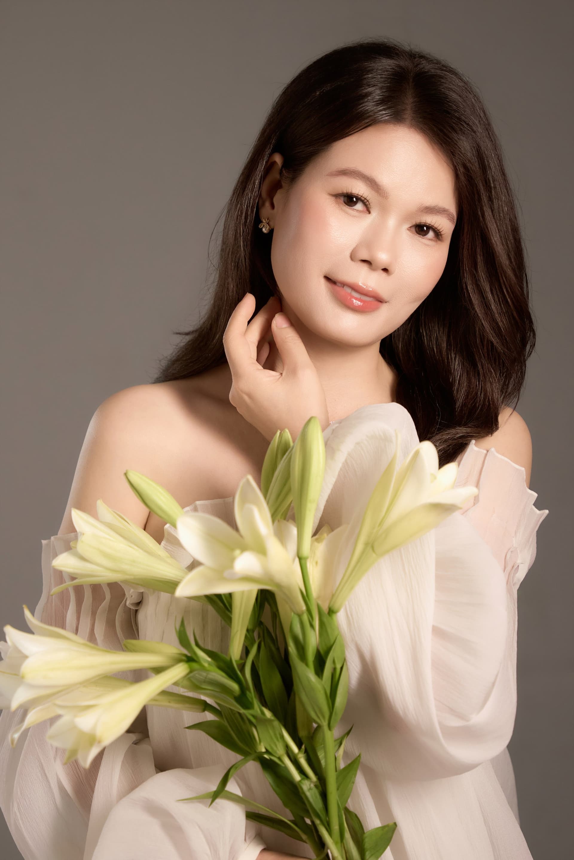 Người phụ nữ ôm bó hoa ly trắng cuống dài, gương mặt nghiêng nhẹ, ánh sáng êm — mong tuổi mới may mắn hơn, nhẹ lòng hơn