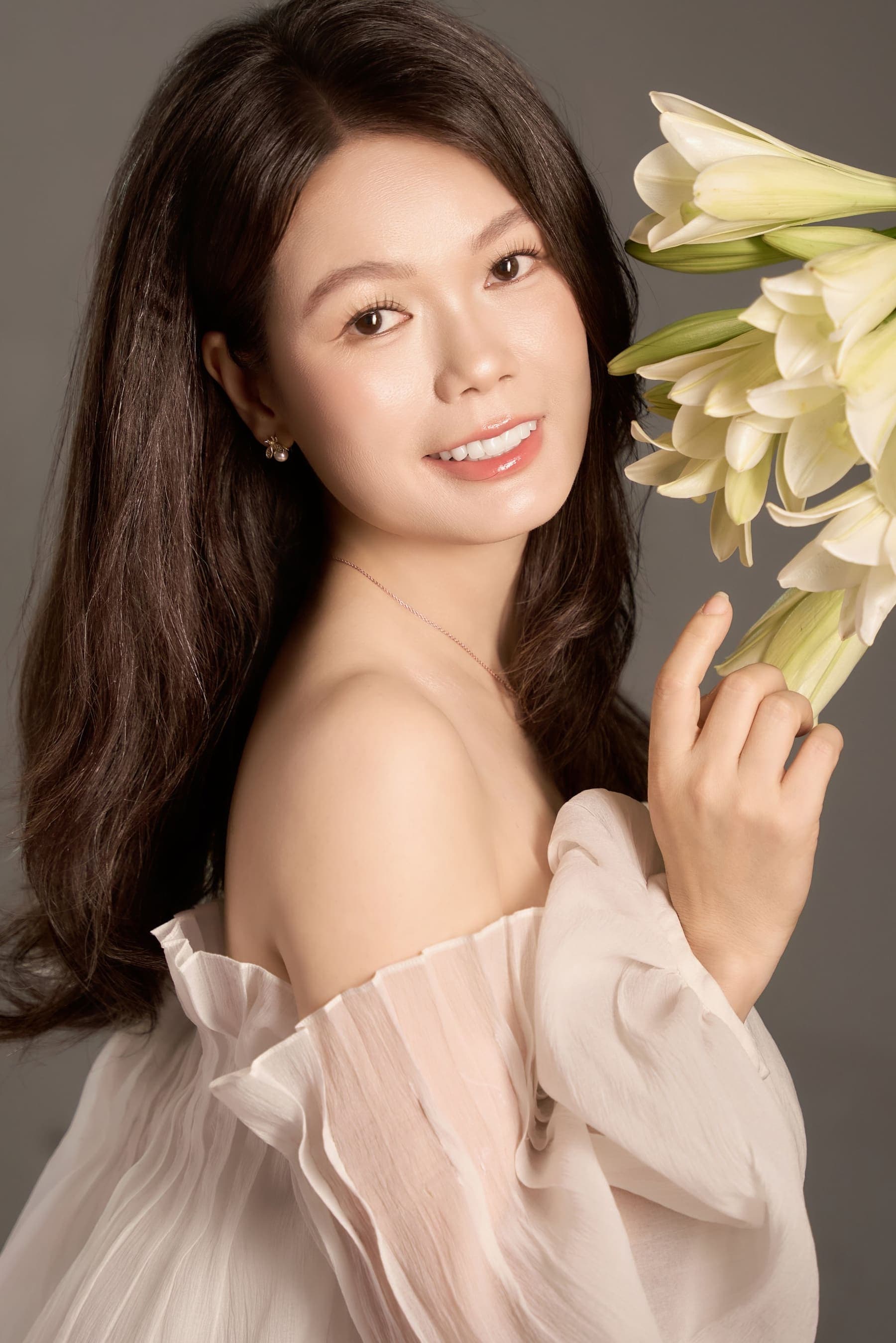 Vũ Huệ ôm hoa, ngón tay khẽ chạm cánh hoa ly trắng, mắt nhìn xuống dịu dàng — một kỷ niệm chị tự giữ cho mình