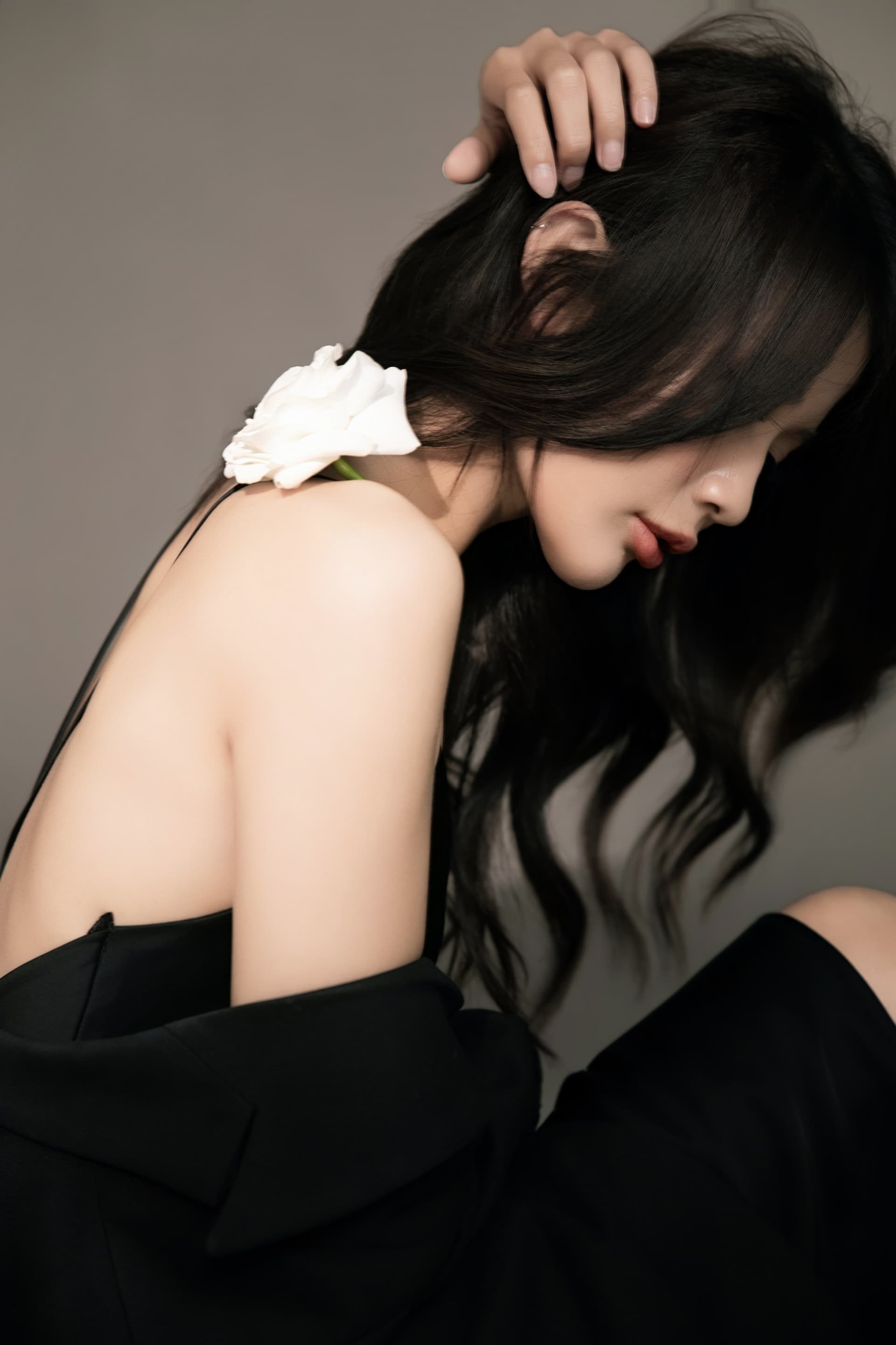 Người phụ nữ trong blazer đen quay lưng, vai trần, một bông hồng trắng cài tóc — chân dung dư âm, không lộ mặt