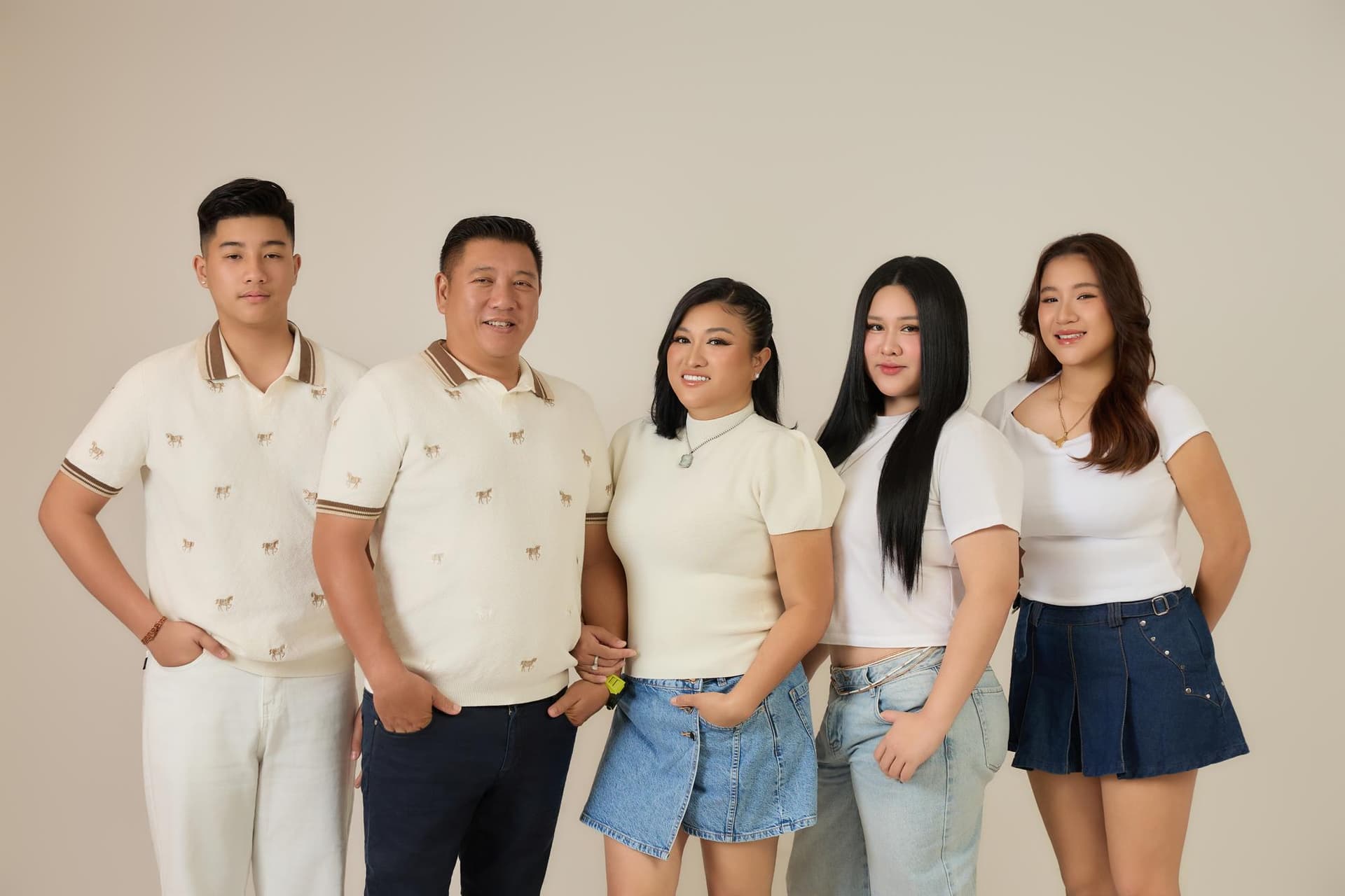 Gia đình năm người đứng cạnh nhau trong trang phục sáng, mỗi người một dáng nhưng cùng chung một mái nhà