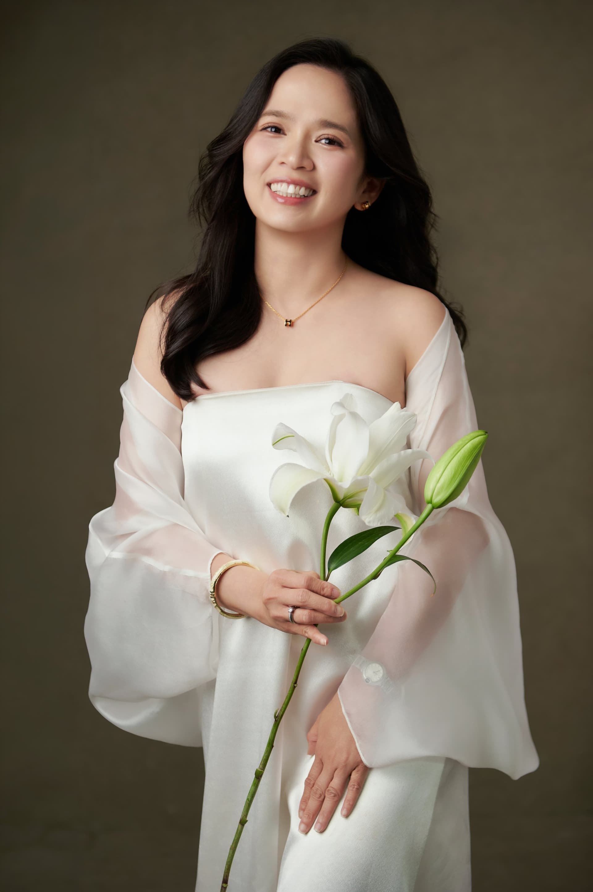 Anh Thi đứng cầm một bông loa kèn trắng — món quà thời gian con gái đặt vào tay mẹ