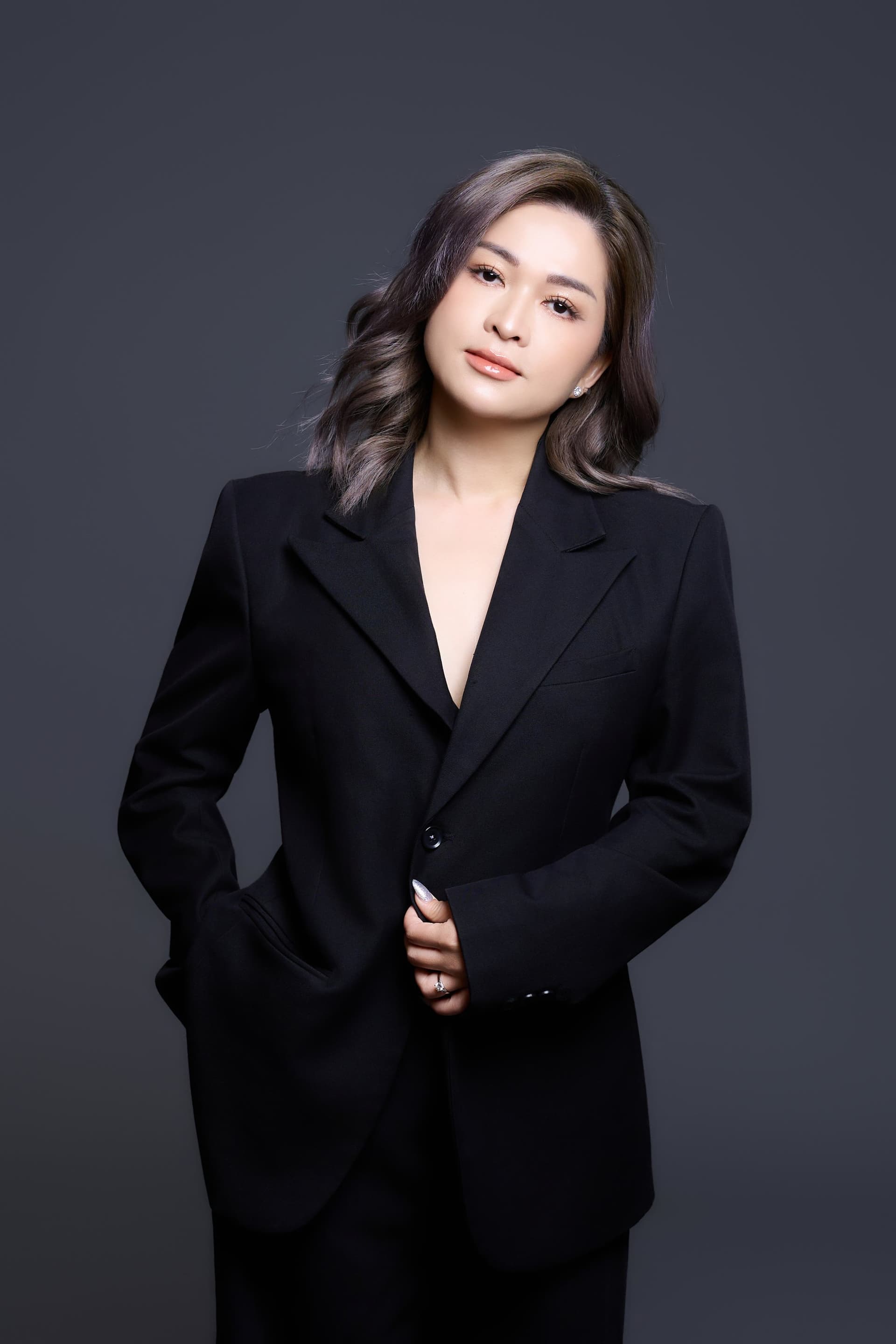 Người phụ nữ đứng một mình trong suit đen, tay vắt sau lưng, ánh nhìn bình thản — sau một lần rủ không có ai cùng được