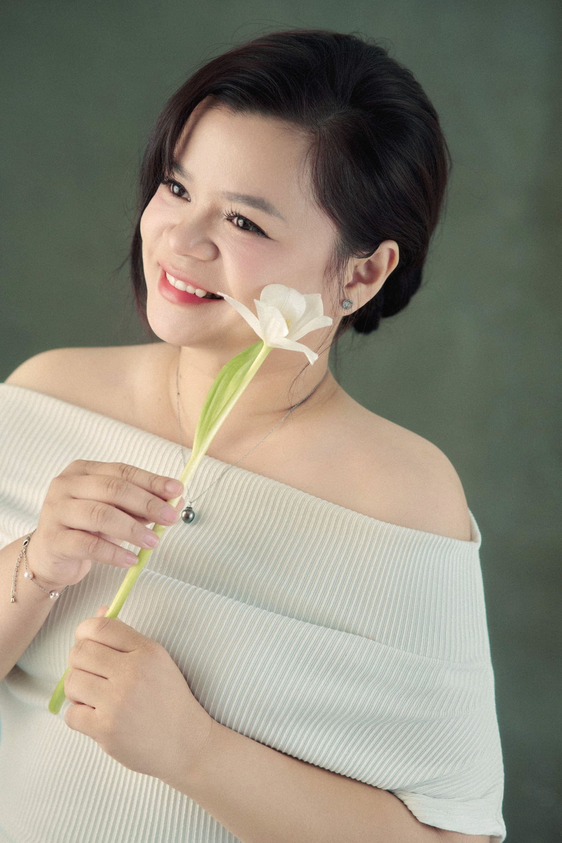 Người phụ nữ vai trần mỉm cười dịu nhìn lên, ôm bó tulip trắng trước ngực — lần đầu dừng lại đón niềm vui của riêng mình
