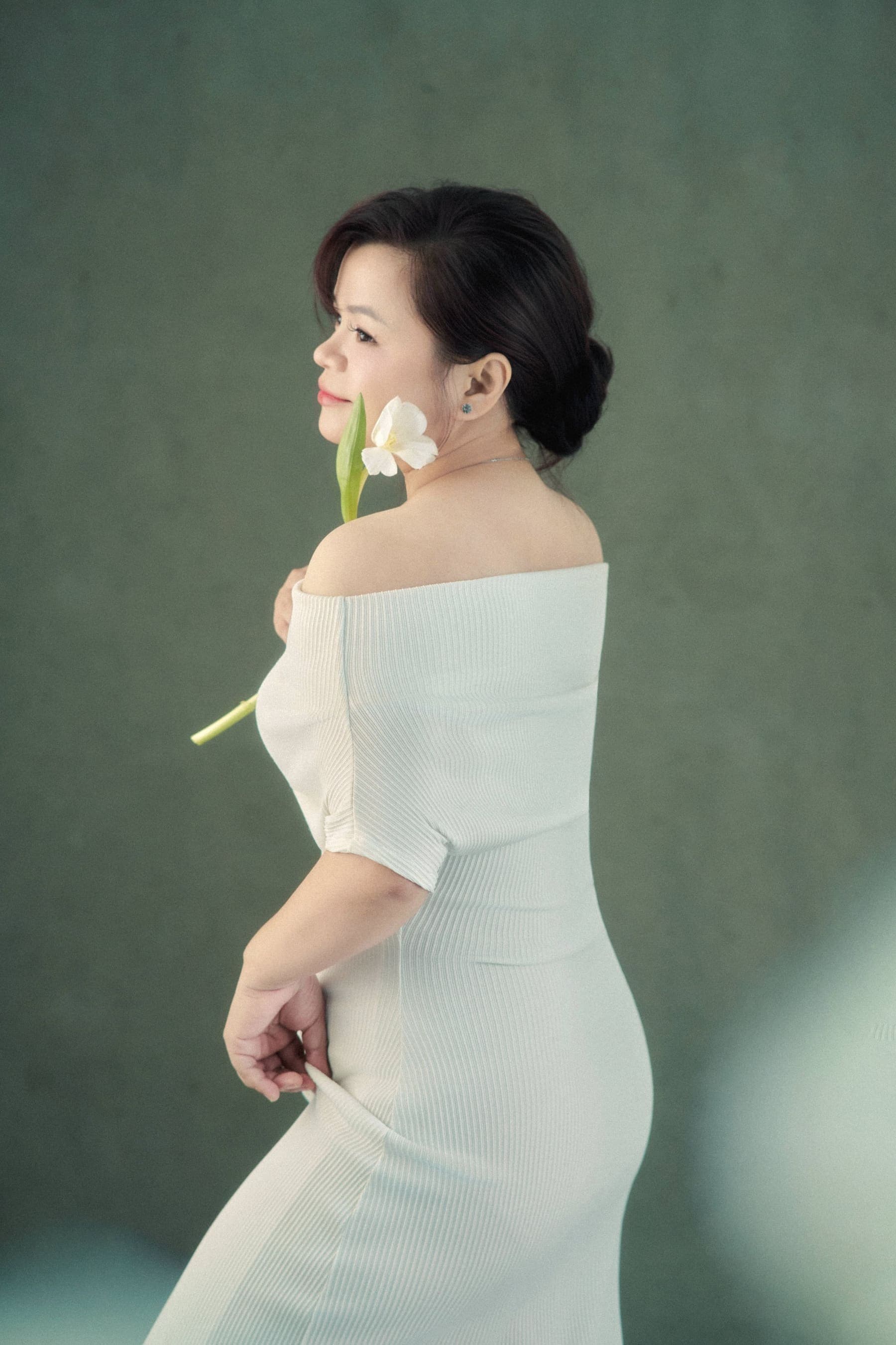 Người phụ nữ trong váy trắng quay lưng nhẹ về phía sau, vai dài thanh — một phần mềm được cất lại sau những ngày phải làm người lớn