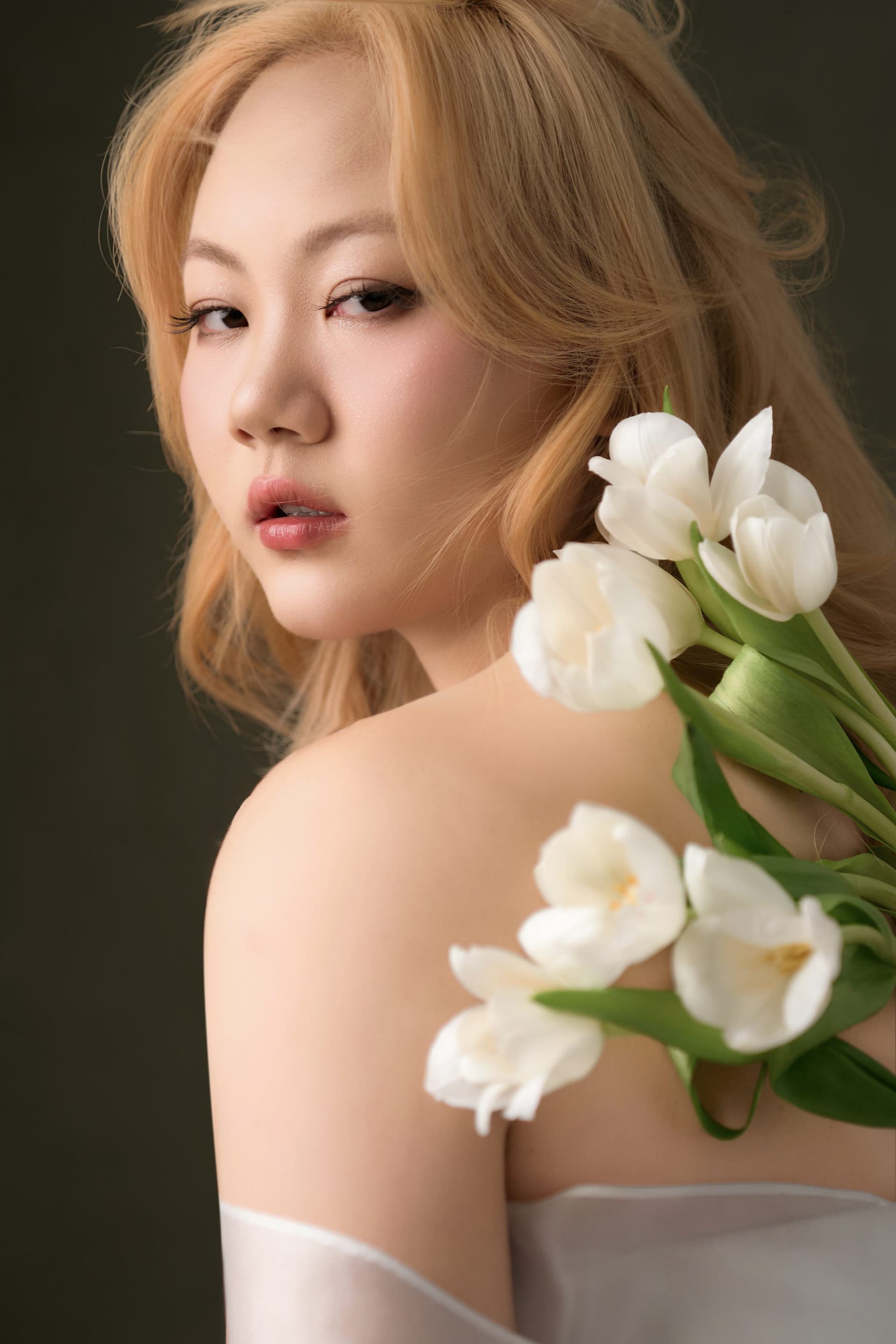 Ri holding white blossoms close to her shoulder, the new hair color softened inside a memory of her own