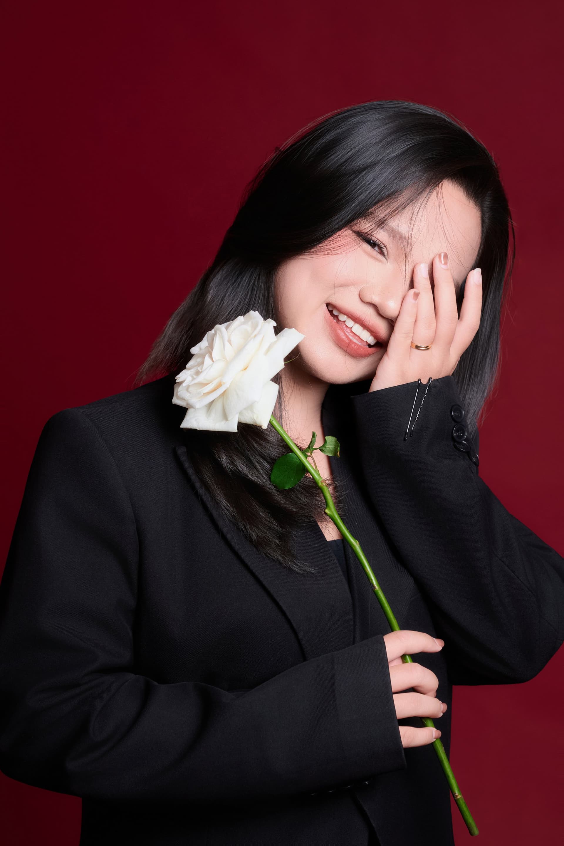 Ms Tiny Nguyễn mỉm cười đầy tinh nghịch, che một bên mắt bên đóa hoa hồng trắng tinh khôi
