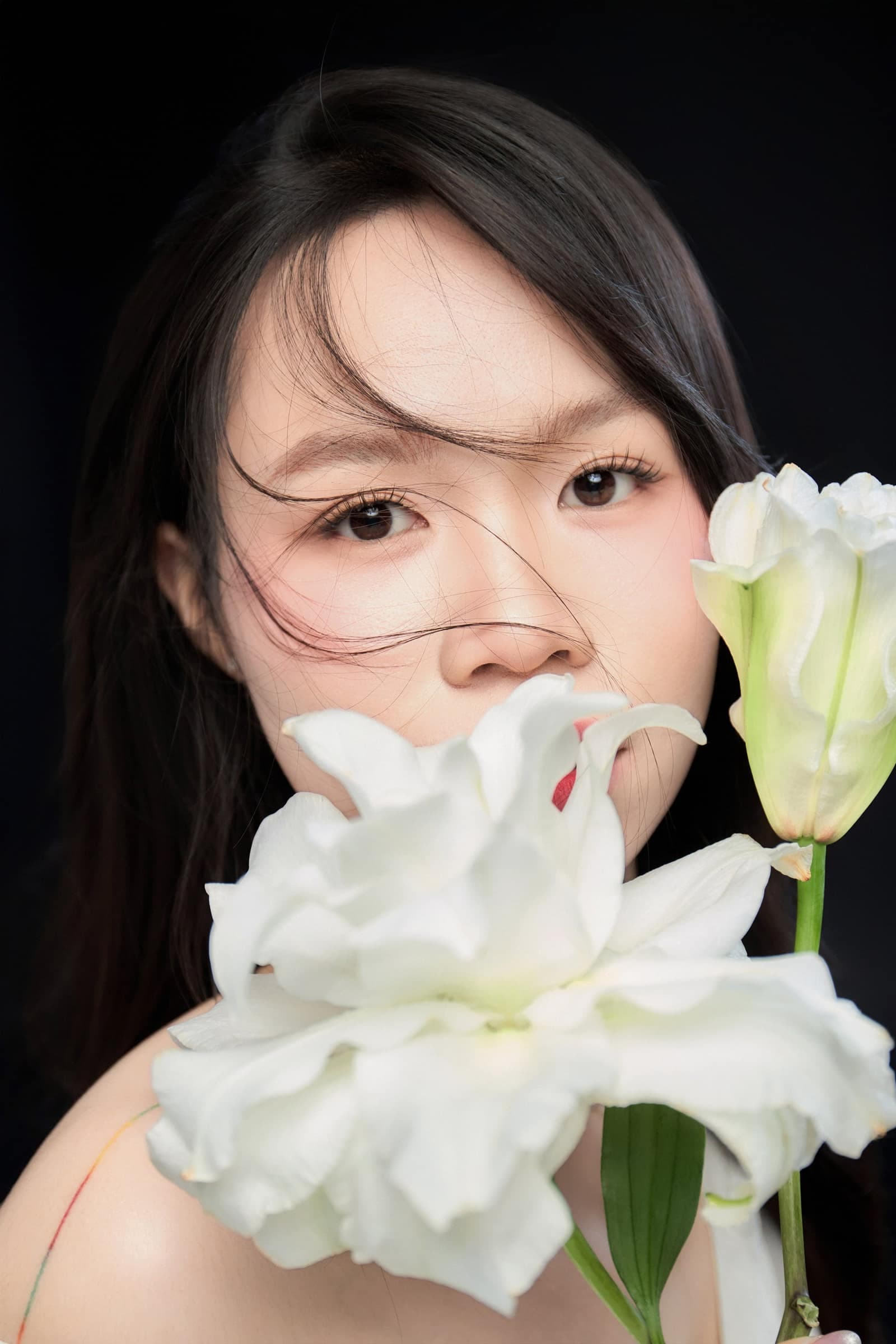 Cô gái ôm bó hoa lily trắng lên mặt, mắt khẽ khép — dáng dịu của một mùa còn xanh, còn nhiều thời gian