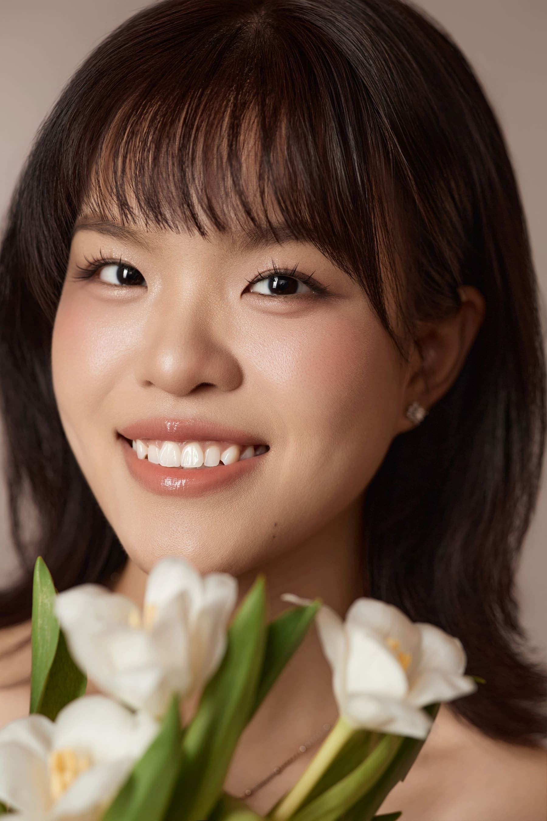 Cận mặt người phụ nữ tóc ngắn, nụ cười rạng rỡ, cầm hoa tulip trắng cạnh vai — khoảnh khắc một mình của Ngọc