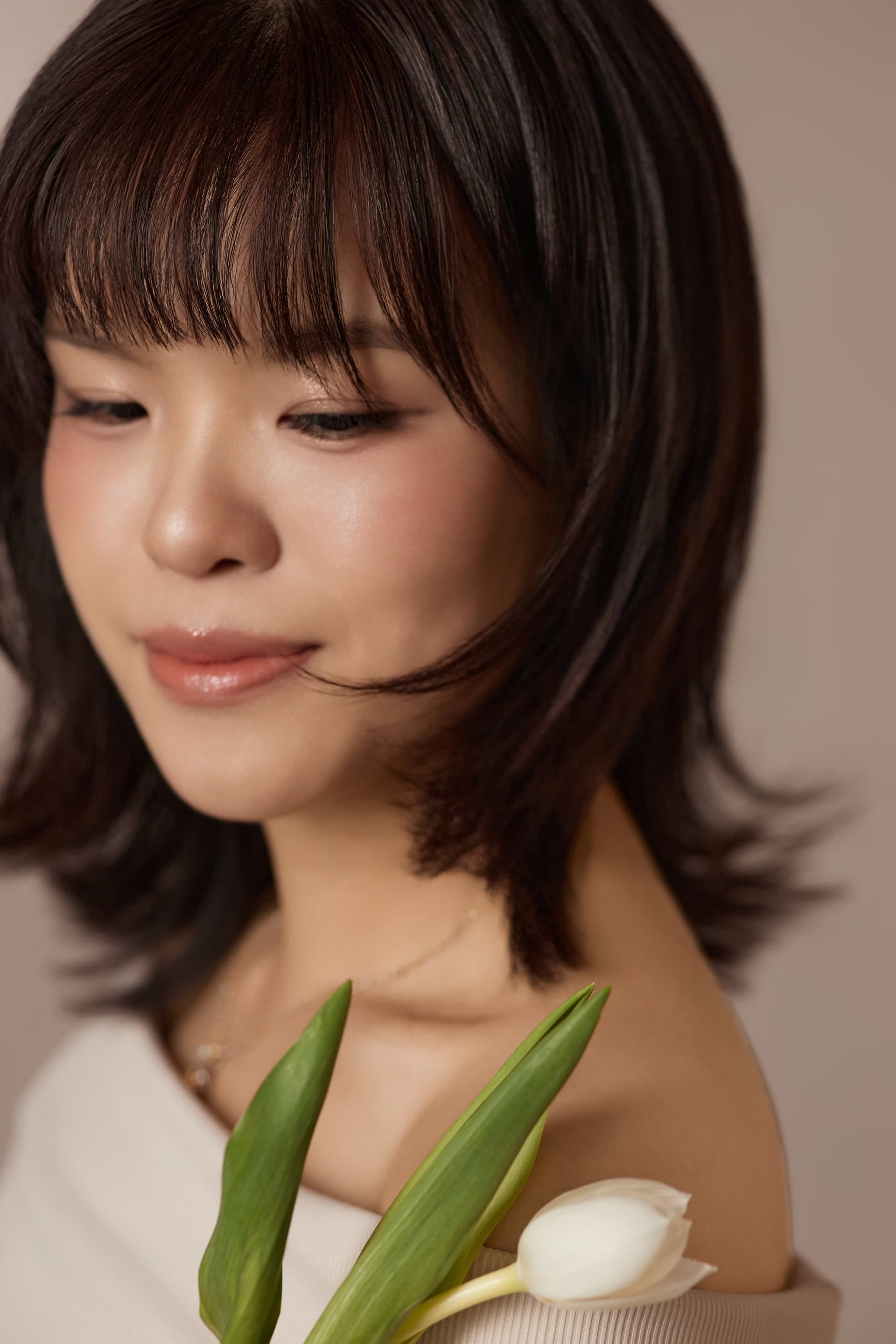 Cận mặt người phụ nữ mắt nhìn xuống nhẹ, môi khẽ cười, hoa tulip trắng bên má — phút chiêm nghiệm về mình