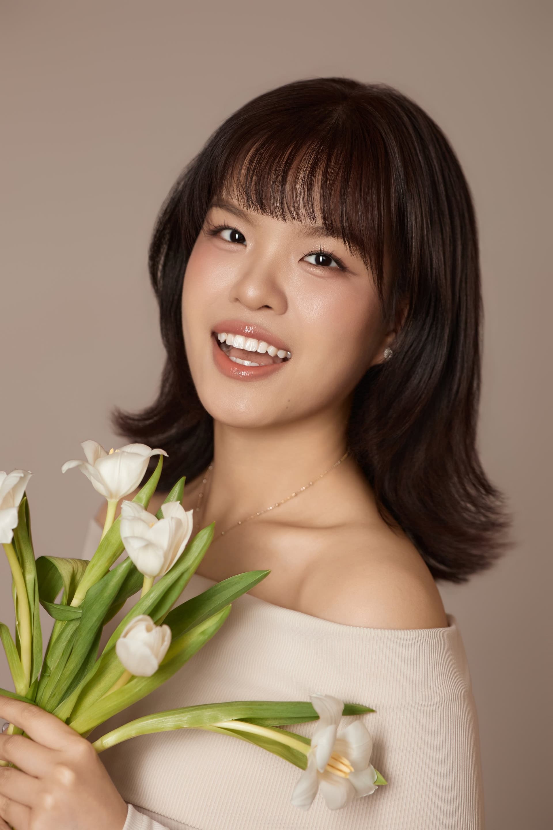 Người phụ nữ áo trắng trễ vai, đứng ôm bó hoa tulip trắng, miệng cười tươi — phần dịu dàng được mở lại