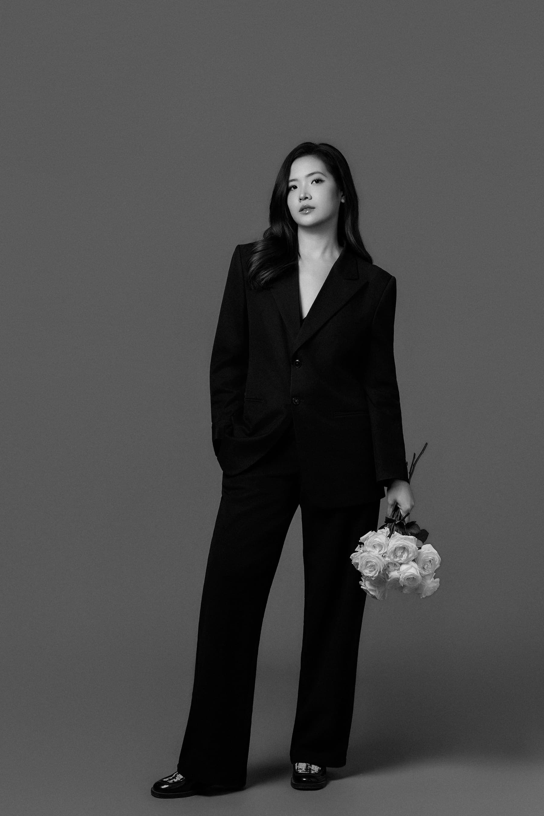 Phương Uyên dáng đứng tiến về phía trước, suit blazer đen ôm bó hoa trắng, người phụ nữ sau sinh được xếp lại