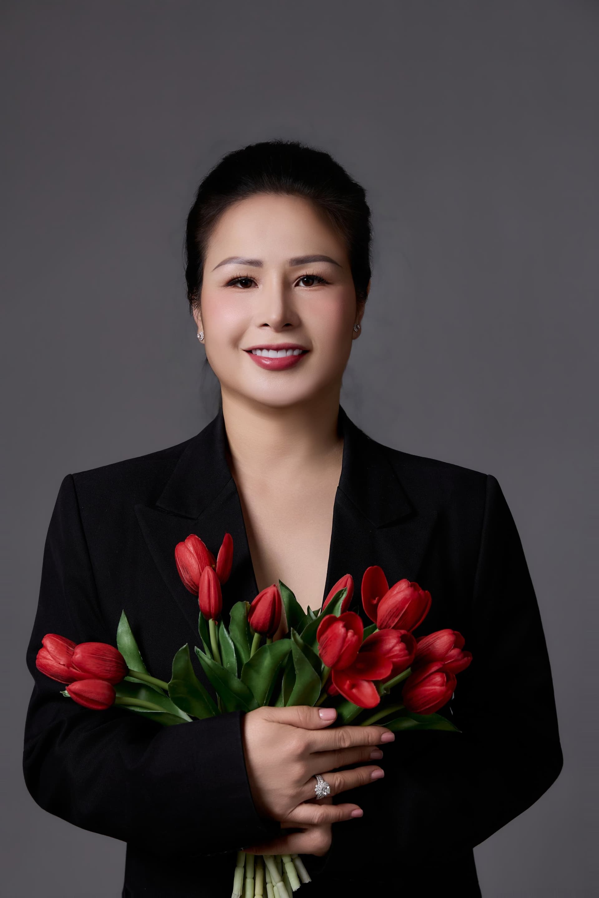 Người phụ nữ ôm bó tulip đỏ trong vest đen — dáng đứng đàng hoàng của một người vừa trở về với việc của riêng mình