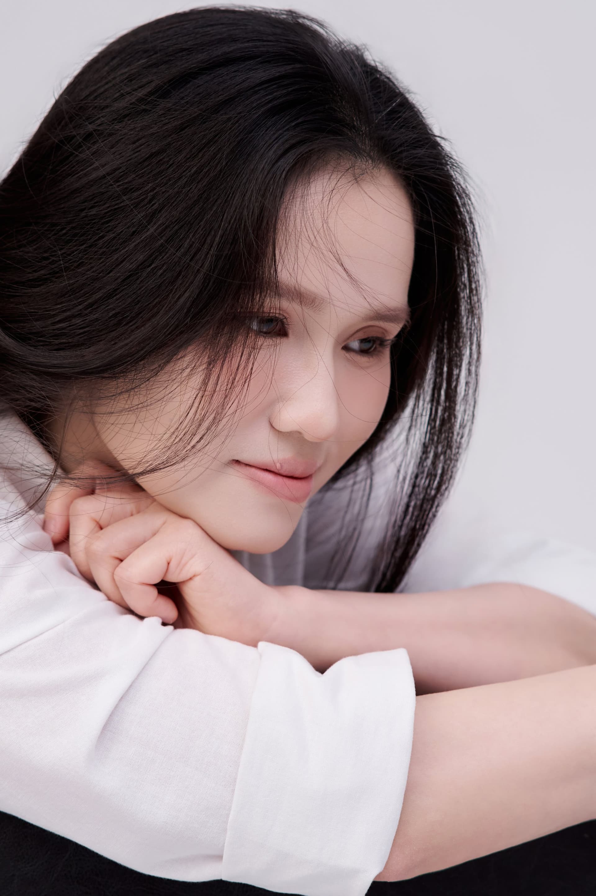 Khánh Huyền mặc váy trắng nằm nghiêng mình trên giường gỗ, ánh mắt mơ màng, tĩnh lặng.