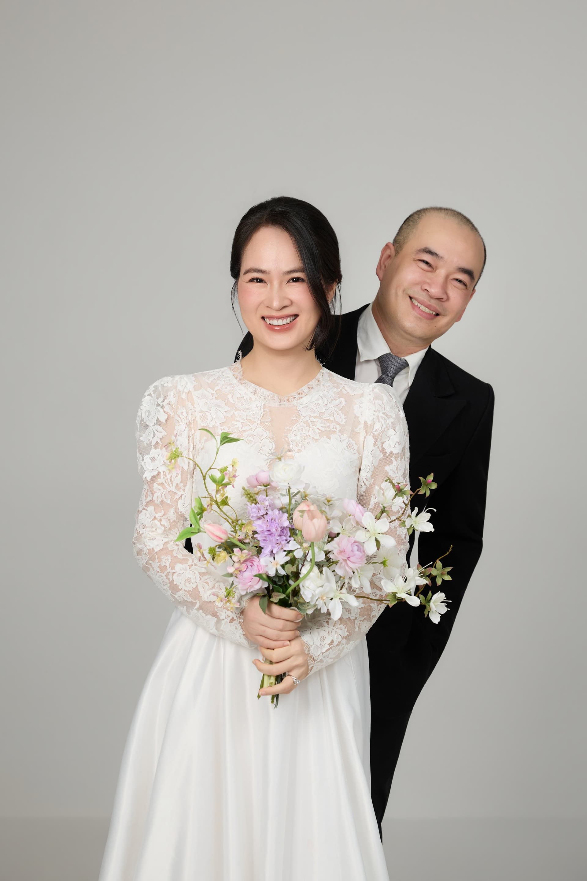 Cô dâu váy trắng và chú rể mặc vest đen ôm eo nhau cười rạng rỡ hạnh phúc