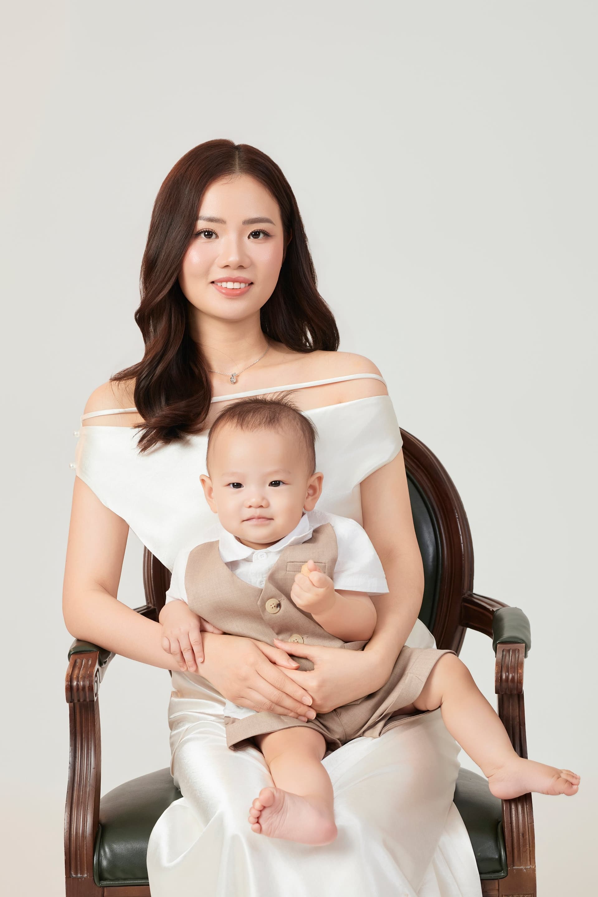 Người mẹ ôm con trong lòng đầy trìu mến bên cạnh người cha đang mỉm cười