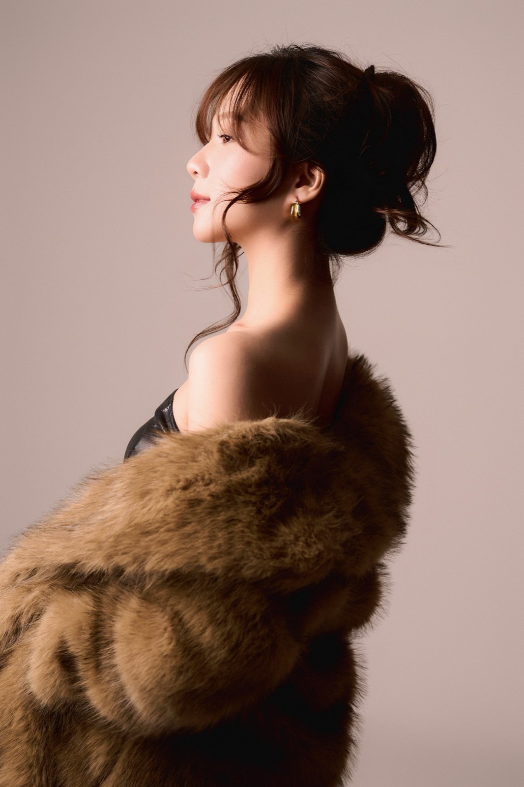 Sắc Ly nhìn nghiêng, áo lông nâu phủ vai, tóc búi cao, môi đỏ — một khuôn mặt bình tĩnh hơi quá so với tuổi.