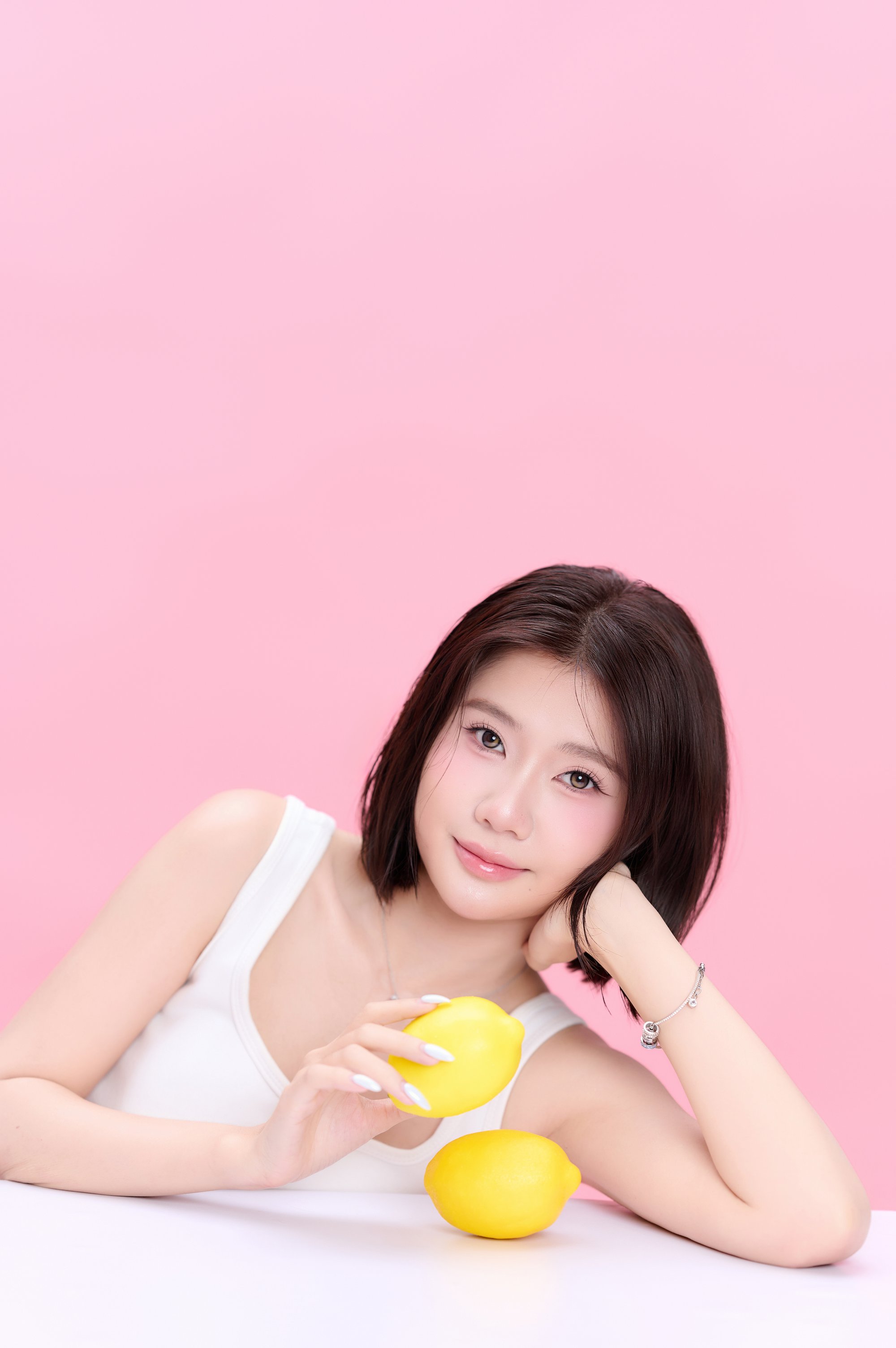 Phương tank top trắng, hai tay ôm chanh vàng nền hồng