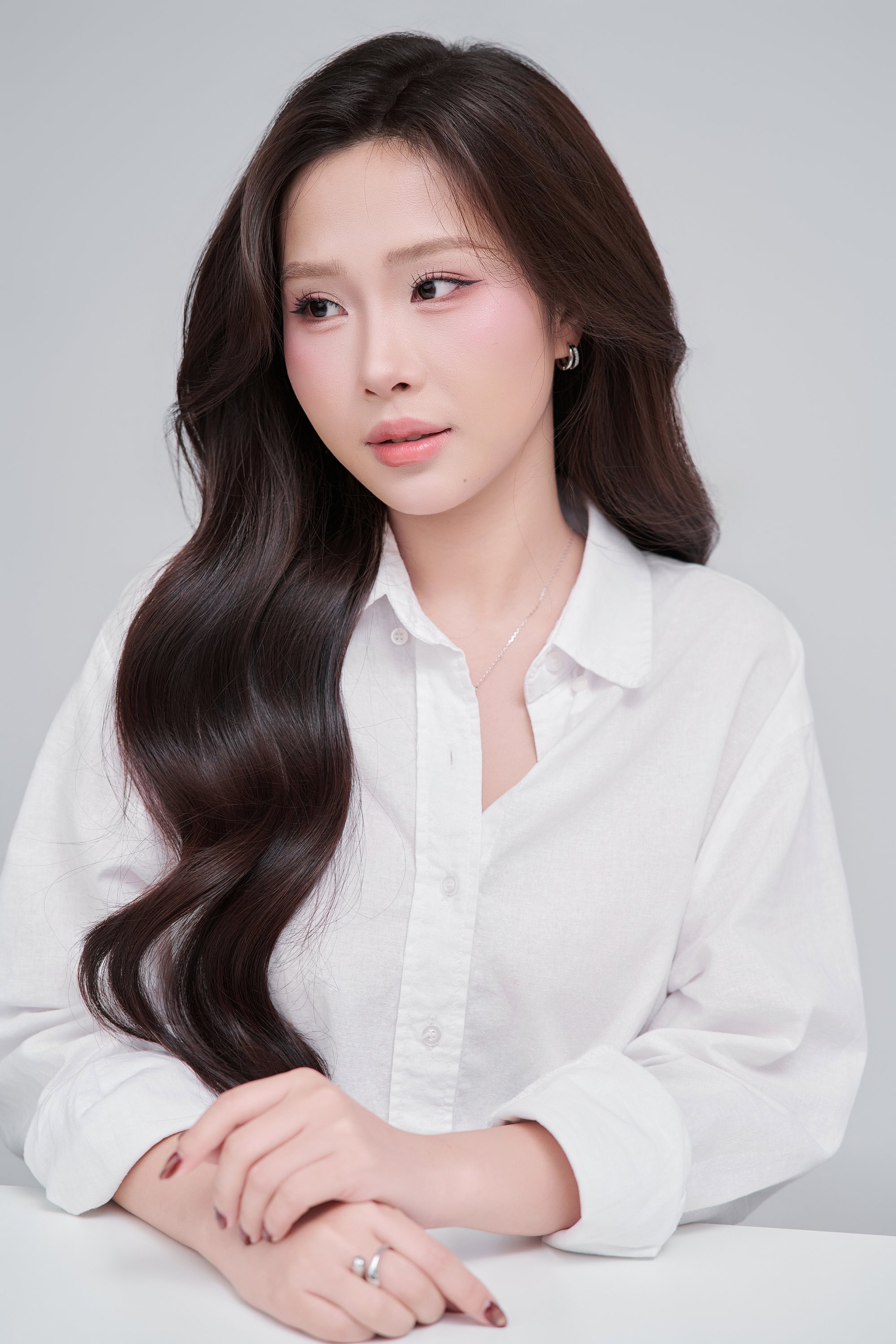 Cận chân dung thiếu nữ áo sơ mi trắng, hai tay đan vào nhau đặt trên bàn, móng sơn nâu đậm, ánh nhìn dịu xuống — khoảnh khắc "thả" của câu chuyện