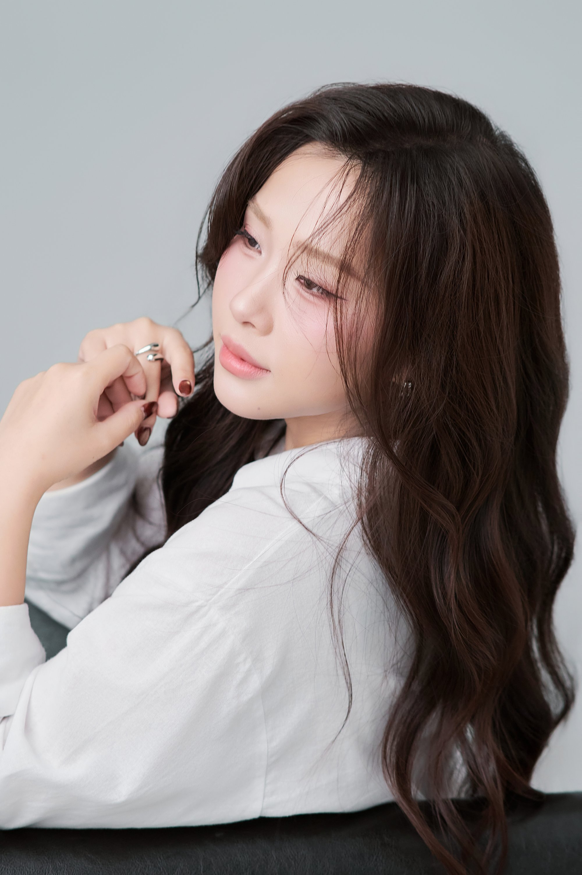 Thiếu nữ áo sơ mi trắng nhìn nghiêng qua vai, tóc dài buông sóng, tay chạm vào tóc, ánh mắt mơ màng — bản dạng "áo trắng dịu"