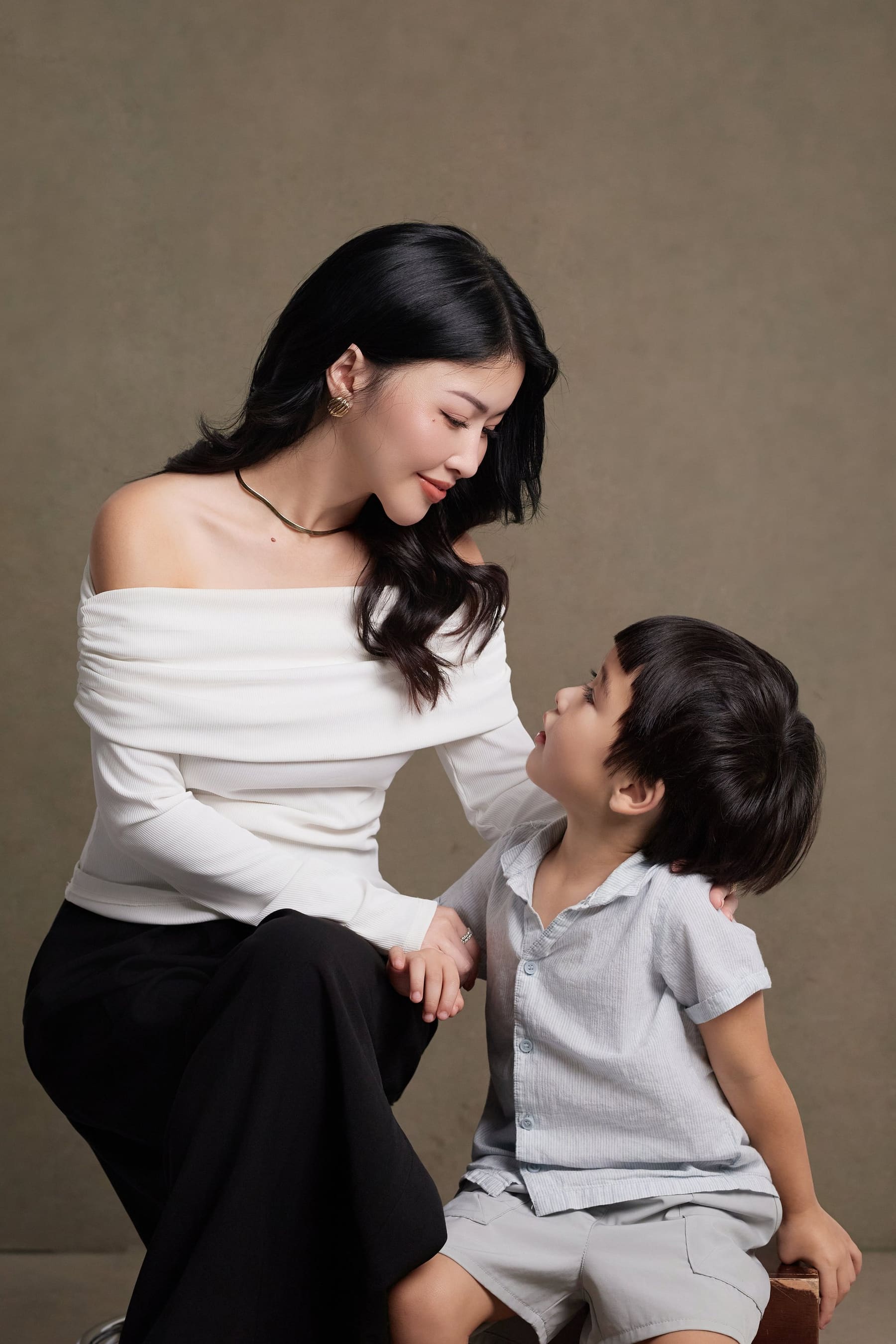 Trang nghiêng người về phía con trai nhỏ, hai mẹ con nhìn nhau, bàn tay con đặt vào lòng mẹ — một phần đời bé xíu đang lớn lên cùng mẹ
