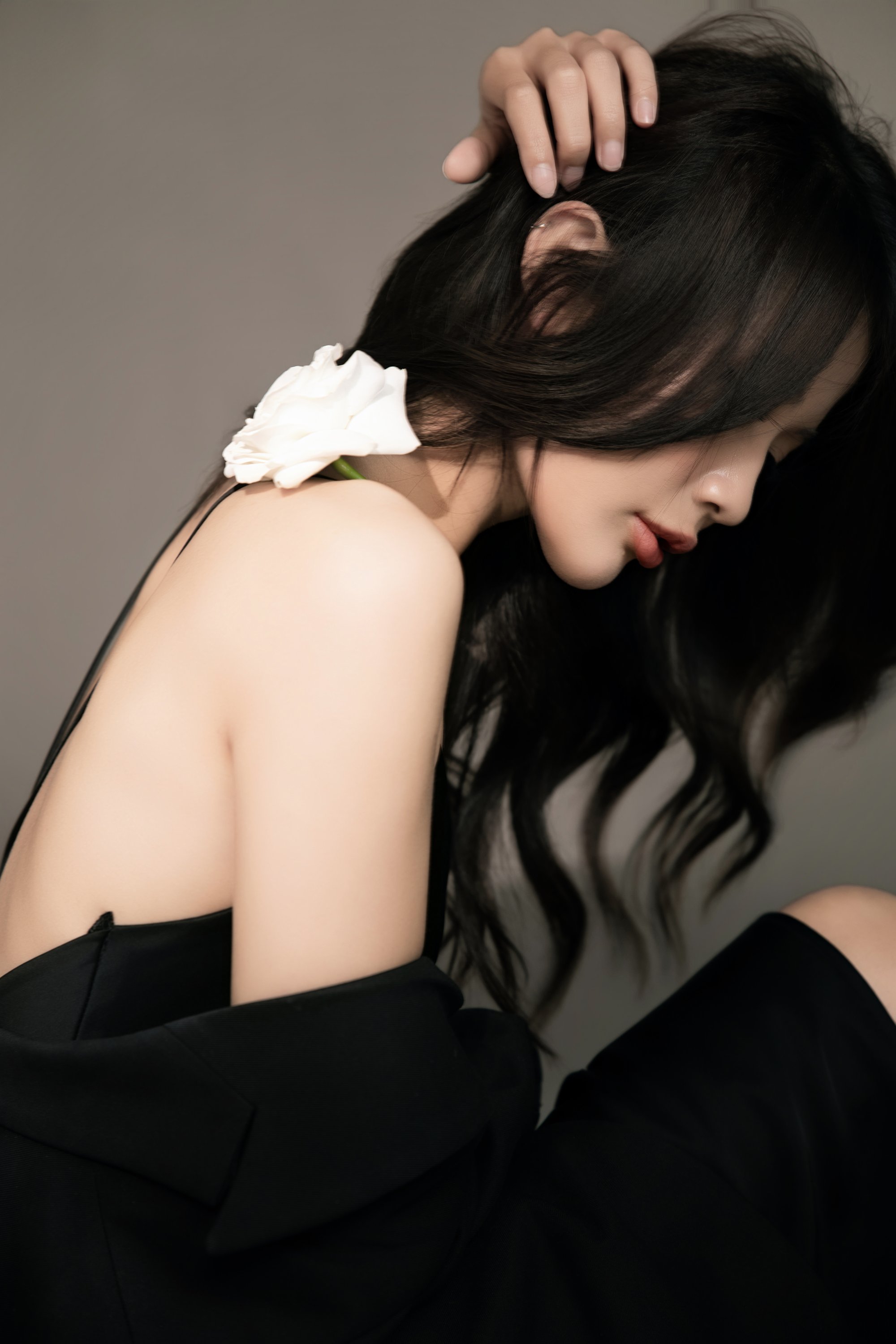 Người phụ nữ trong blazer đen quay lưng, vai trần, một bông hồng trắng cài tóc — chân dung dư âm, không lộ mặt
