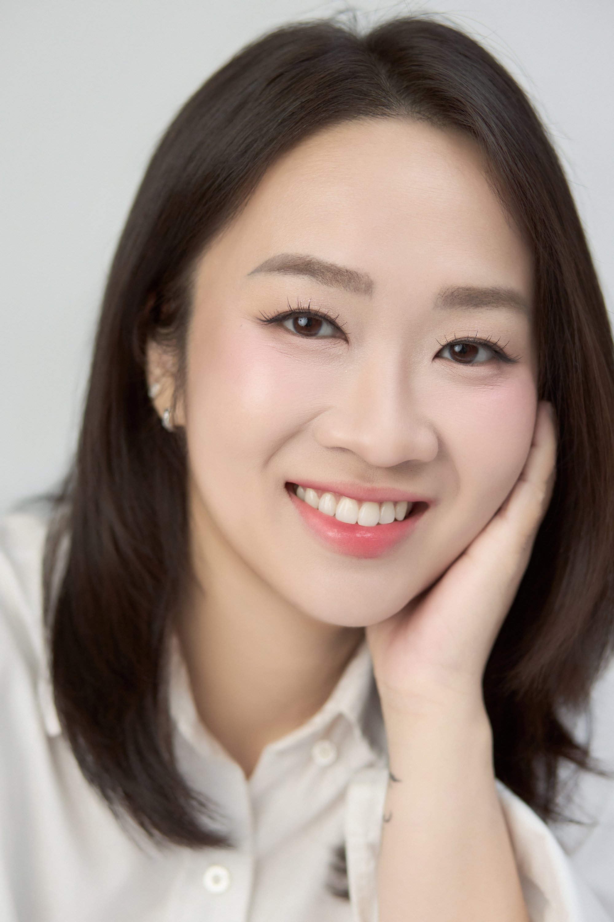 Trần Ngọc Minh Trâm áo sơ mi trắng, một tay đỡ má, nụ cười rạng rỡ — gương mặt của một ngày tự cho phép mình dừng lại