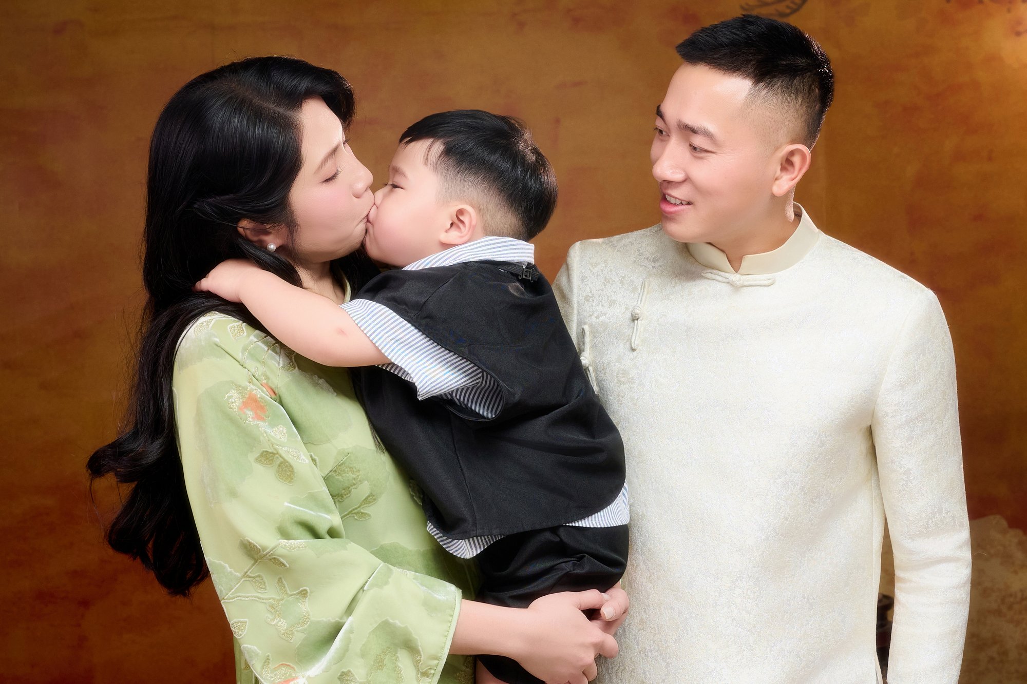 Khoảnh khắc cha mẹ áp má, hôn lên má con nhỏ — cả nhà chụm vào nhau trong một khung hình ngang