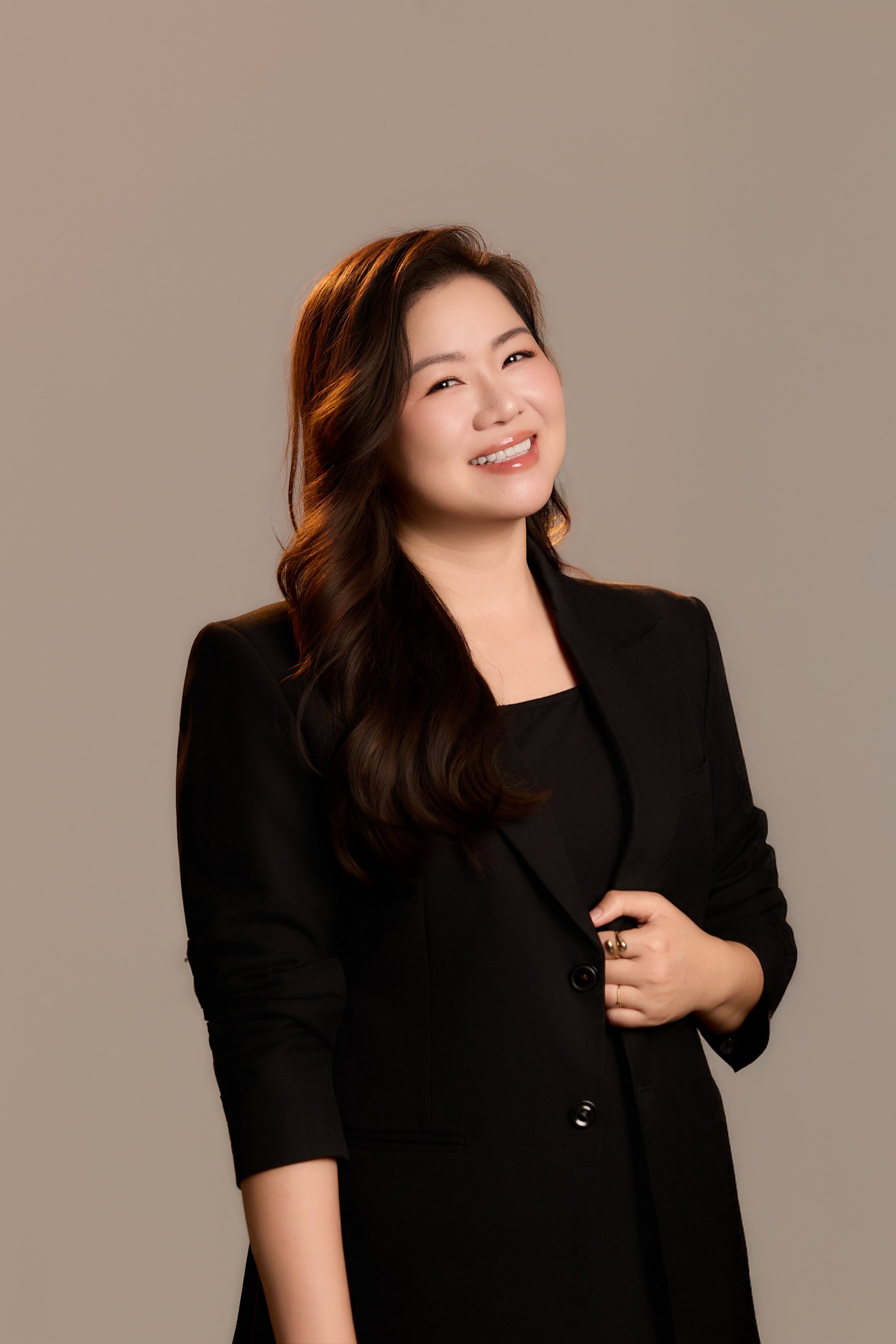 Trang Ngo đứng thẳng trong vest đen, cười cởi mở — gương mặt của hôm nay, của một người vẫn đang ở đây
