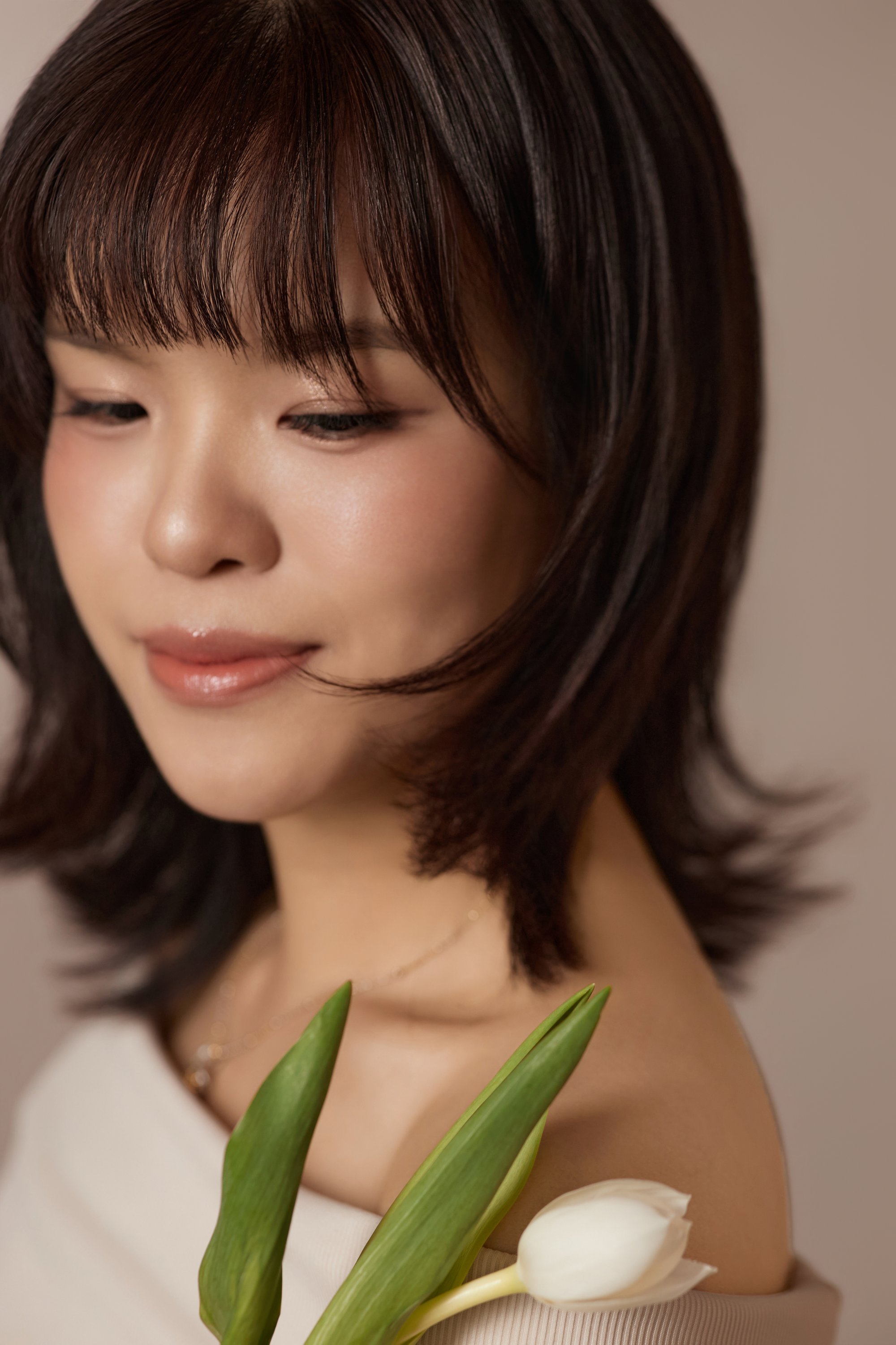 Cận mặt người phụ nữ mắt nhìn xuống nhẹ, môi khẽ cười, hoa tulip trắng bên má — phút chiêm nghiệm về mình