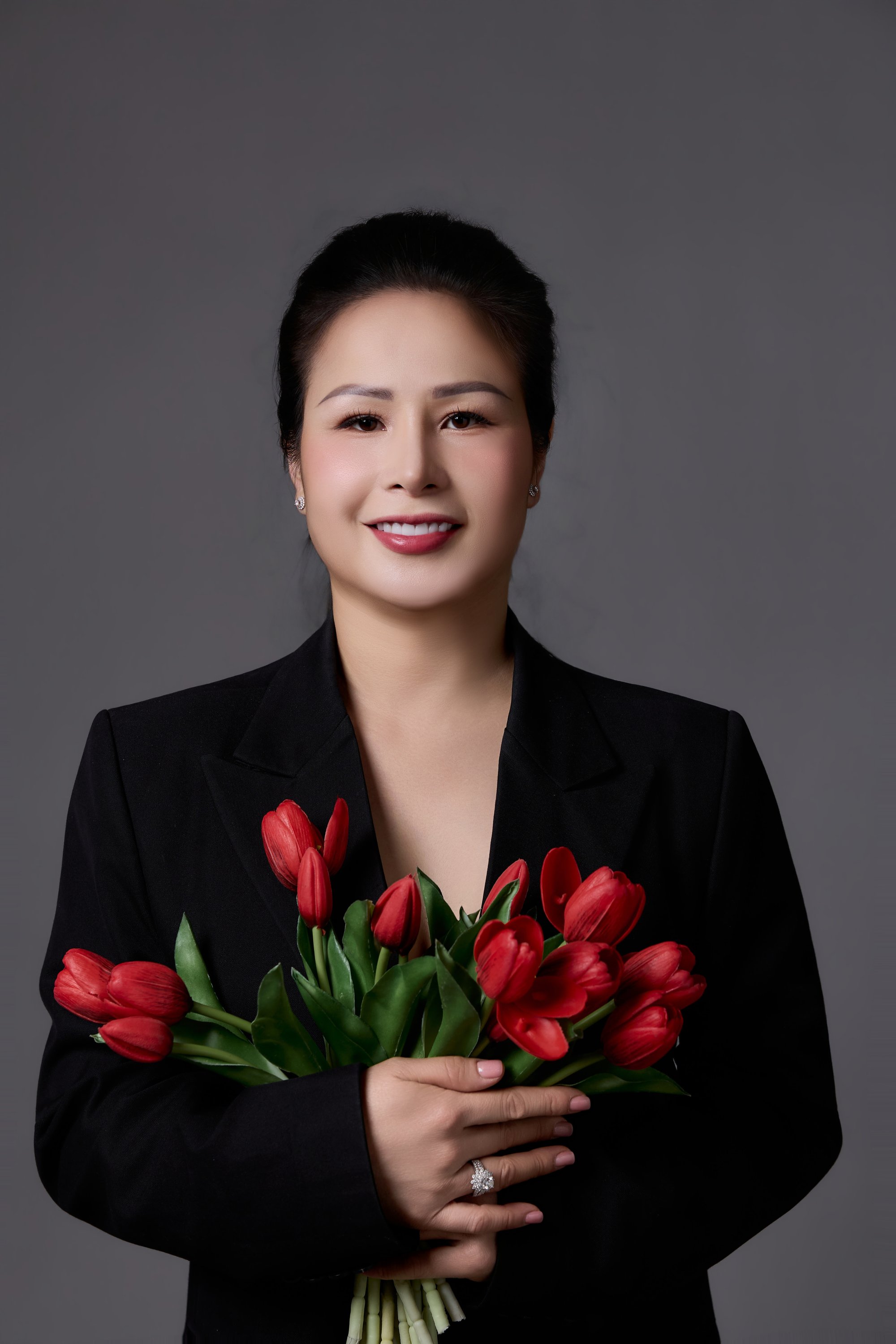 Người phụ nữ ôm bó tulip đỏ trong vest đen — dáng đứng đàng hoàng của một người vừa trở về với việc của riêng mình